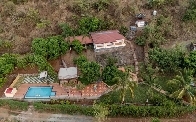 Redroof Farmhouse and its pool from above, on a wooded hillside